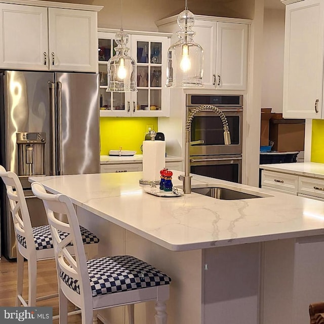 kitchen featuring white cabinets, appliances with stainless steel finishes, glass insert cabinets, a breakfast bar area, and hanging light fixtures