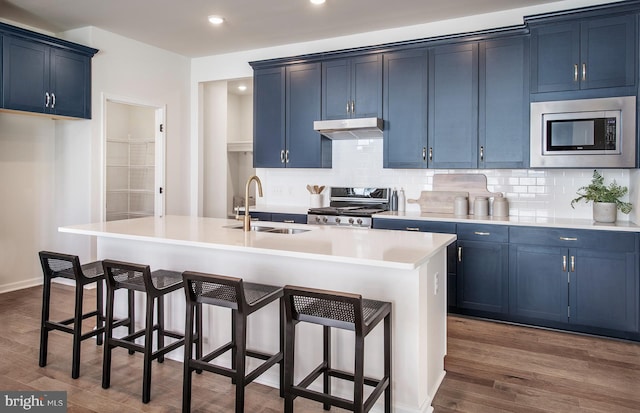 kitchen featuring dark wood-type flooring, stainless steel appliances, an island with sink, and blue cabinets