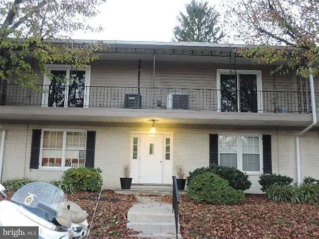 view of property featuring central AC, brick siding, and a balcony