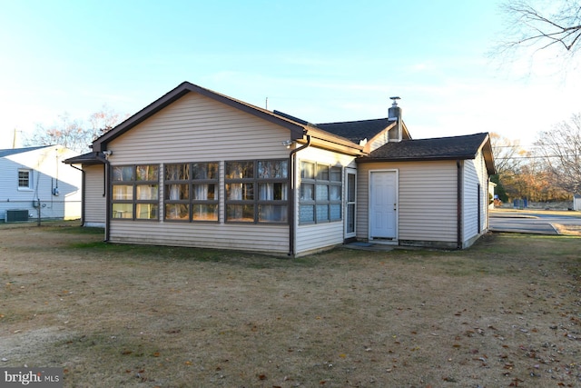 back of property with a sunroom, central AC unit, and a lawn