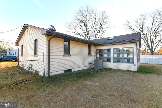 rear view of house featuring central AC and a lawn