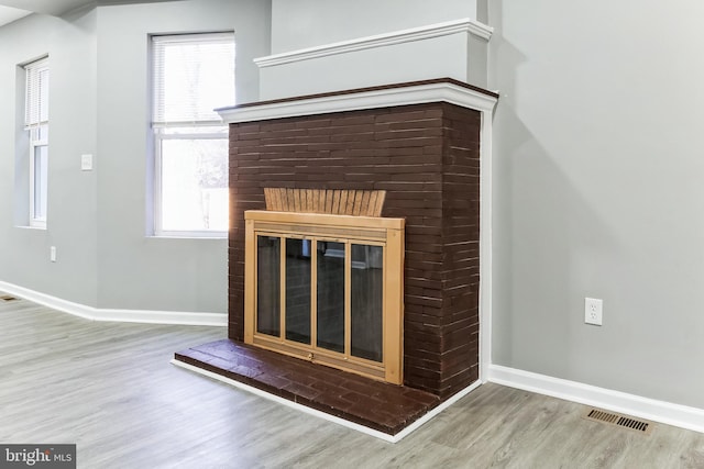 interior details featuring a brick fireplace, visible vents, baseboards, and wood finished floors