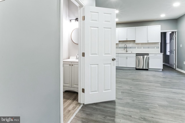 kitchen with light countertops, backsplash, light wood-style flooring, stainless steel dishwasher, and white cabinetry