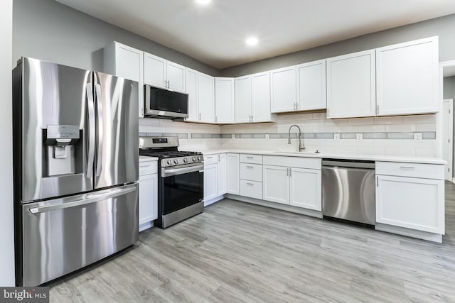 kitchen with light wood finished floors, stainless steel appliances, light countertops, backsplash, and a sink