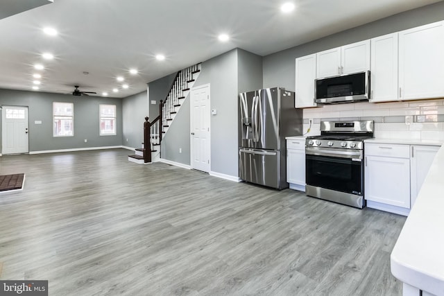 kitchen with light wood-style flooring, recessed lighting, white cabinets, appliances with stainless steel finishes, and tasteful backsplash