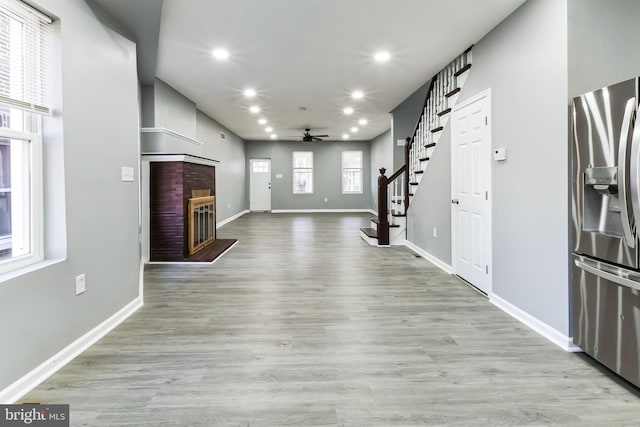 unfurnished living room with a brick fireplace, stairs, baseboards, and wood finished floors