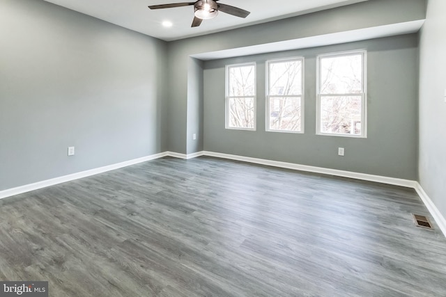 unfurnished room with ceiling fan, visible vents, baseboards, and dark wood finished floors