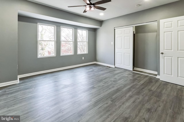 unfurnished bedroom with dark wood-style flooring, a closet, a barn door, ceiling fan, and baseboards