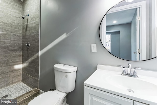 bathroom with toilet, a tile shower, and vanity