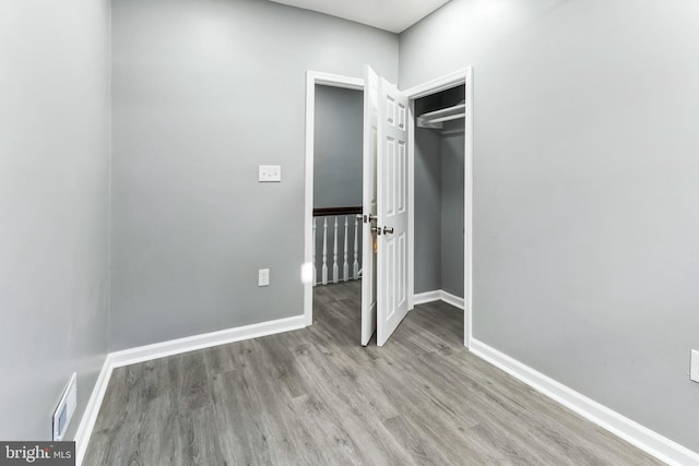 unfurnished bedroom with a closet, visible vents, baseboards, and wood finished floors