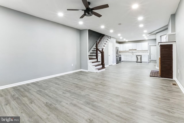 unfurnished living room with baseboards, a sink, light wood finished floors, and stairs