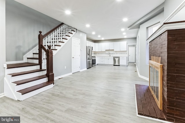 unfurnished living room featuring recessed lighting, a sink, baseboards, stairs, and light wood finished floors