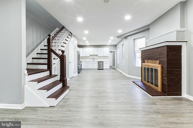 unfurnished living room featuring a fireplace, stairway, light wood-style flooring, a sink, and baseboards