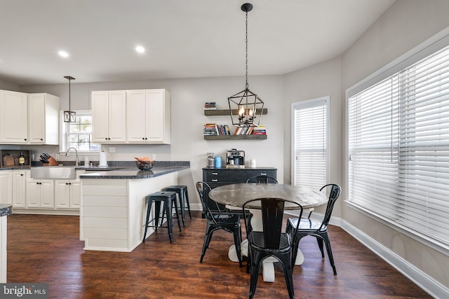 kitchen with decorative light fixtures, a breakfast bar area, sink, white cabinets, and dark hardwood / wood-style floors