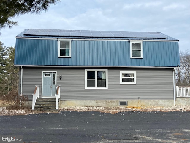 view of front facade with entry steps, roof mounted solar panels, metal roof, and a gambrel roof