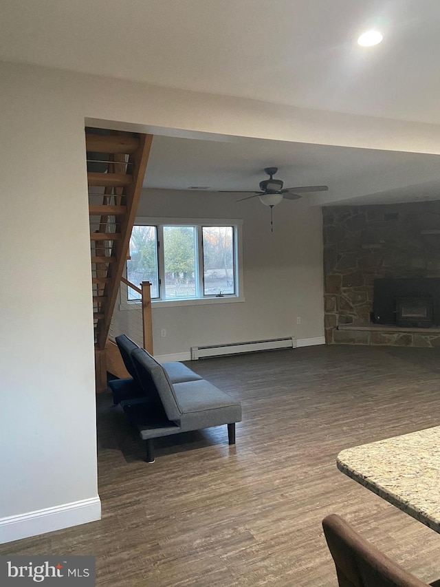 interior space featuring baseboards, ceiling fan, dark wood-style flooring, baseboard heating, and a stone fireplace