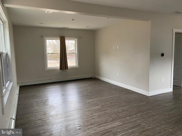 spare room featuring a baseboard radiator, baseboards, and dark wood finished floors