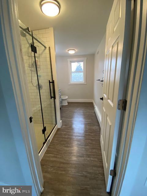 full bathroom featuring a stall shower, wood finished floors, toilet, and baseboards