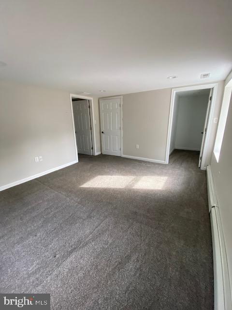 interior space featuring a baseboard radiator, baseboards, and dark colored carpet