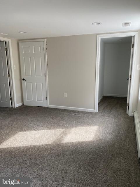 unfurnished room featuring a baseboard heating unit, baseboards, visible vents, and dark colored carpet