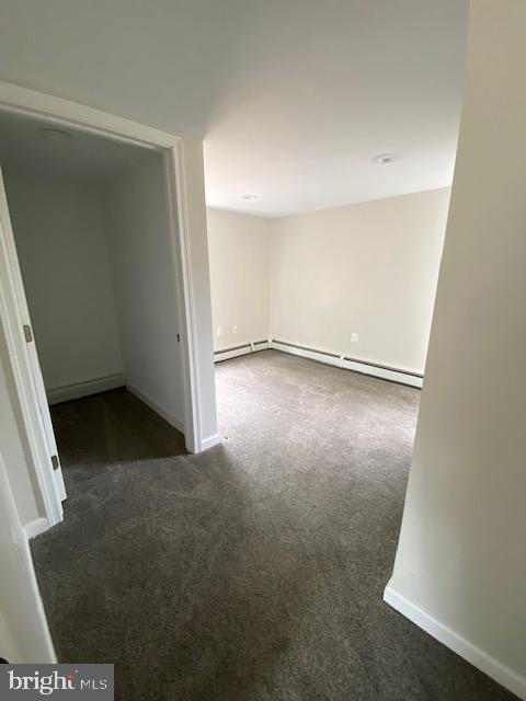 empty room with a baseboard heating unit, baseboard heating, dark carpet, and baseboards