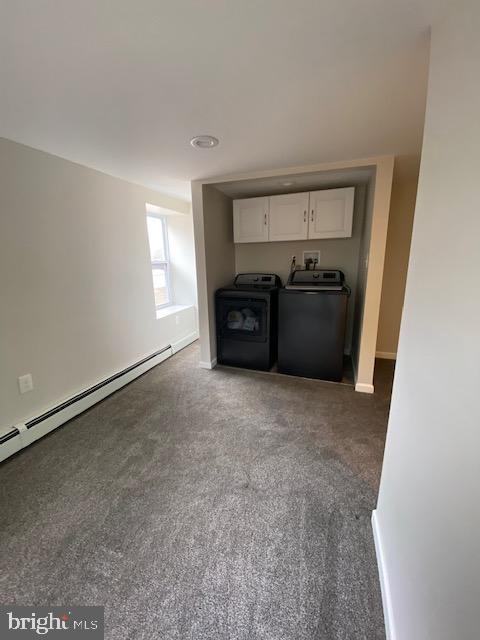 interior space featuring a baseboard heating unit, dark colored carpet, washing machine and dryer, and baseboards