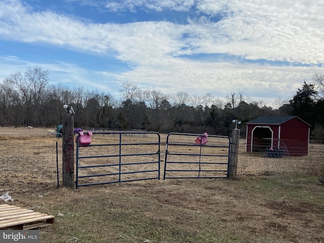 view of gate featuring a rural view, fence, and an outdoor structure