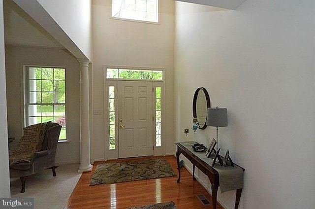 foyer entrance with hardwood / wood-style floors, ornate columns, and a towering ceiling