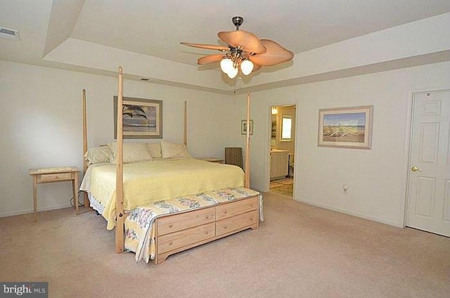 bedroom with a tray ceiling, light carpet, connected bathroom, and ceiling fan