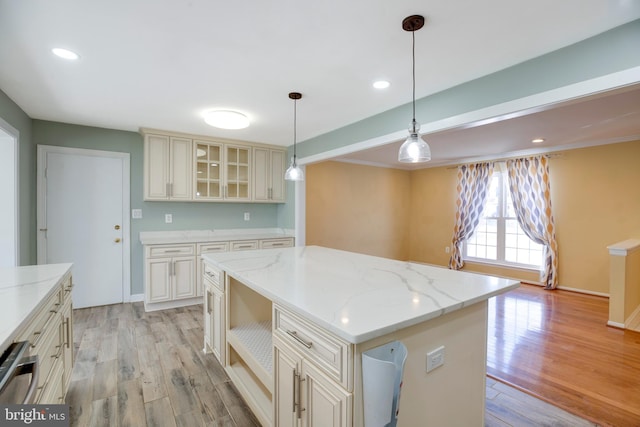 kitchen with cream cabinetry, hanging light fixtures, light stone countertops, light hardwood / wood-style floors, and a center island