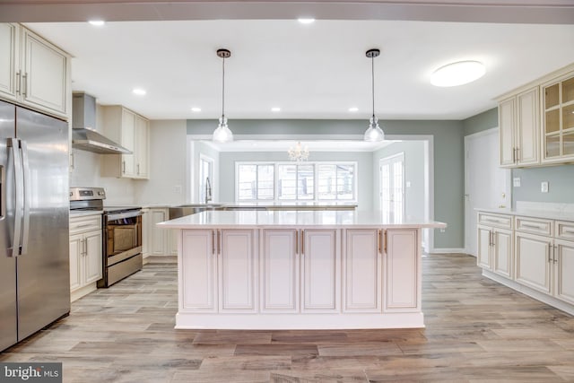 kitchen with wall chimney range hood, hanging light fixtures, stainless steel appliances, and a kitchen island