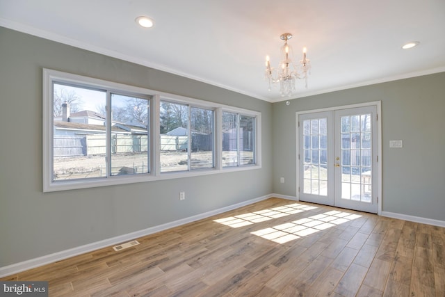 spare room featuring light wood-type flooring, a chandelier, crown molding, and french doors