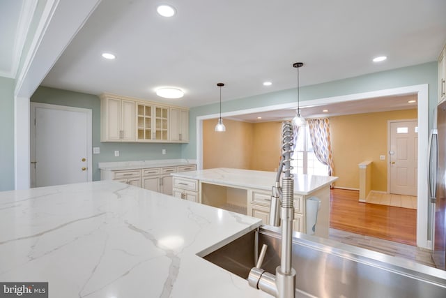 kitchen featuring light wood-type flooring, pendant lighting, cream cabinetry, and light stone counters