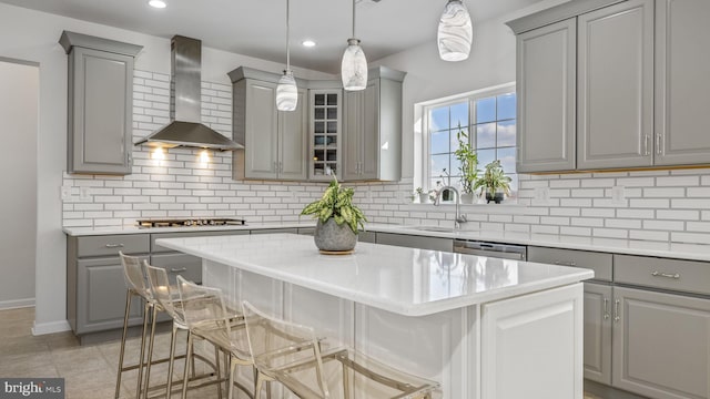 kitchen with a center island, wall chimney exhaust hood, gray cabinetry, and a breakfast bar area