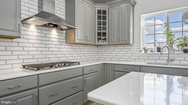 kitchen with gray cabinetry, stainless steel gas stovetop, light stone countertops, exhaust hood, and sink