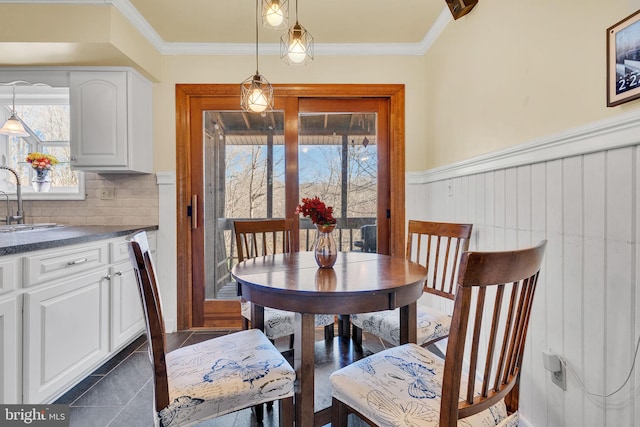 dining room featuring dark tile patterned flooring, crown molding, and a wainscoted wall