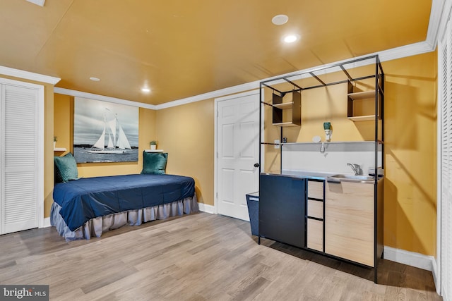 bedroom featuring baseboards, ornamental molding, a sink, and light wood-style floors