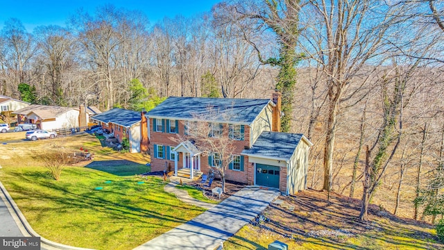 colonial house with a front lawn, an attached garage, a chimney, brick siding, and driveway