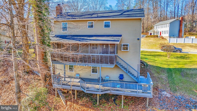 back of house featuring a chimney, stairway, a deck, a yard, and a sunroom