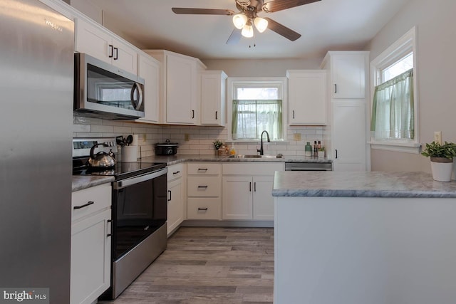 kitchen featuring appliances with stainless steel finishes, sink, backsplash, white cabinetry, and light hardwood / wood-style floors