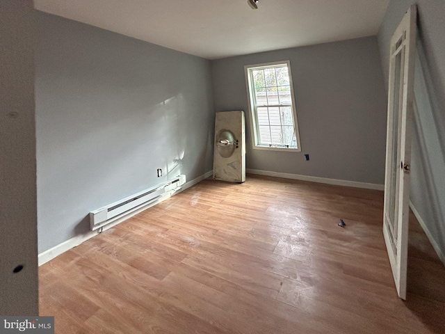 unfurnished bedroom featuring a baseboard heating unit, baseboards, and light wood-style floors