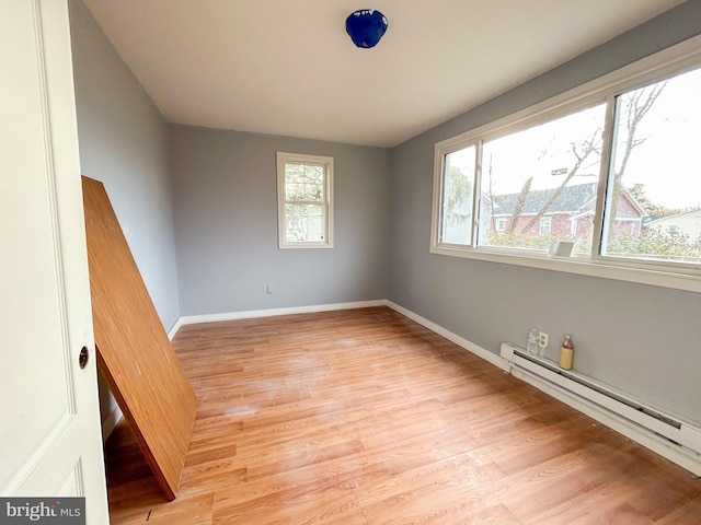 empty room featuring a baseboard radiator, baseboards, and light wood finished floors