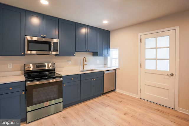 kitchen with stainless steel appliances, blue cabinets, sink, and light wood-type flooring