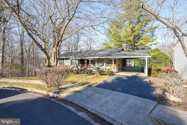 ranch-style home featuring aphalt driveway, a chimney, covered porch, and a carport