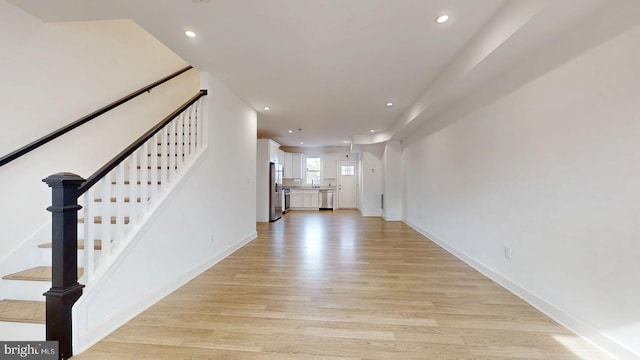 unfurnished living room featuring baseboards, stairway, light wood-style flooring, and recessed lighting