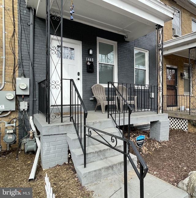 doorway to property featuring covered porch and brick siding