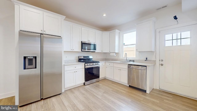 kitchen with stainless steel appliances, a sink, visible vents, light wood-style floors, and light countertops