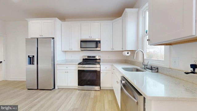 kitchen with white cabinets, light wood-style flooring, stainless steel appliances, and a sink