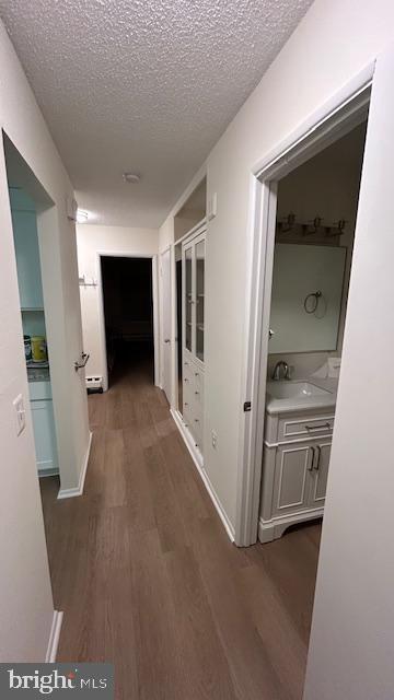 hallway featuring dark wood-type flooring, sink, and a textured ceiling