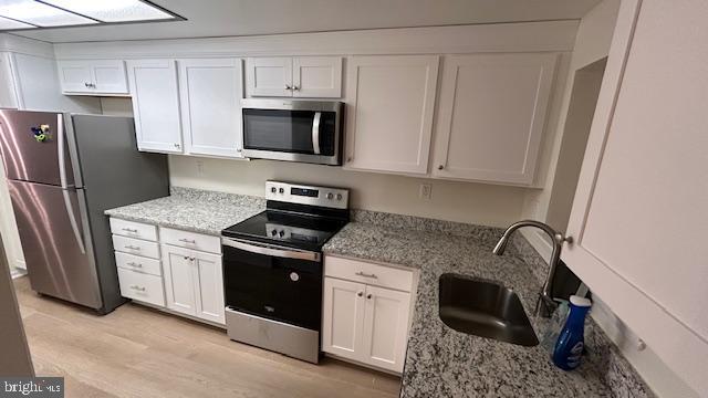 kitchen with white cabinetry, sink, stainless steel appliances, and light stone countertops